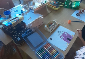 dzieci siedzą przy stolikach i malują farbami